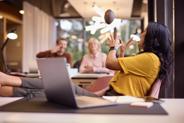 Mature Businesswoman With Feet On Desk In Office Catching Small American Football